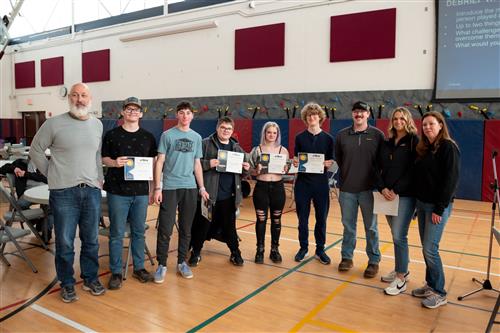  A group of students and adults pose in a gym, holding certificates and smiling at the camera.